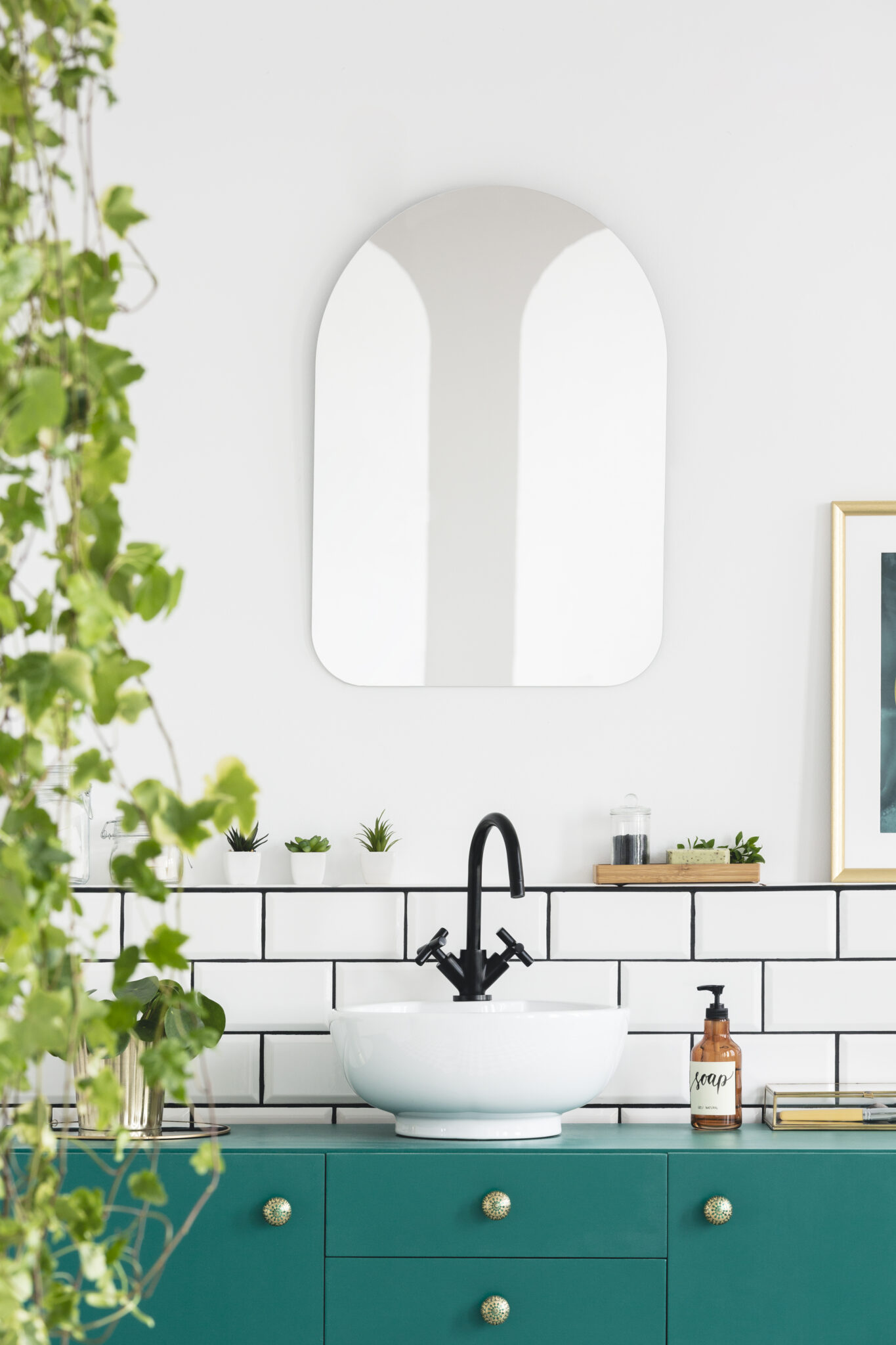 Close-up of leaves with a mirror, wash basin, black faucet and turquoise cupboard in a bathroom interior. Real photo