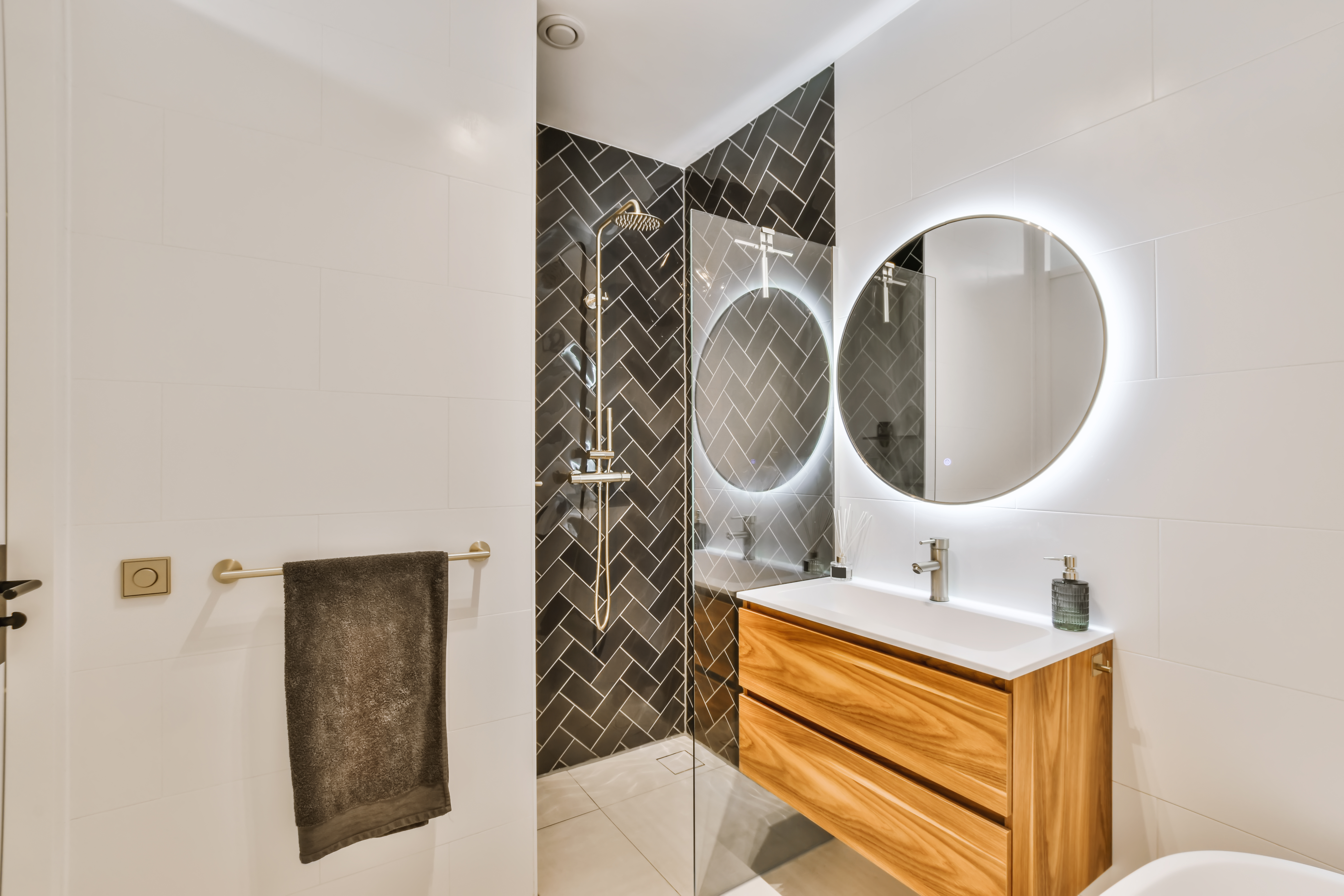 Stunning bathroom with large round illuminated mirror and sink with wooden cabinet